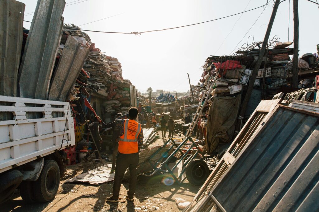 Laborers sorting through scrap metal piles in a bustling industrial yard under bright sunlight.