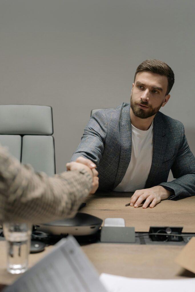 pexels photo 6814528 6814528 Two businessmen in a modern office shaking hands across a table. Professional setting.